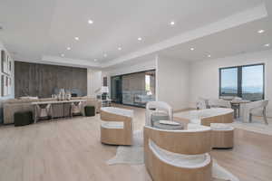 Living room with recessed lighting, light wood-style floors, a raised ceiling, and healthy amount of natural light
