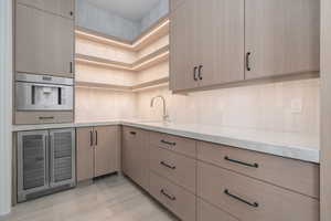 Kitchen with beverage cooler, tasteful backsplash, open shelves, light stone counters, and light brown cabinets