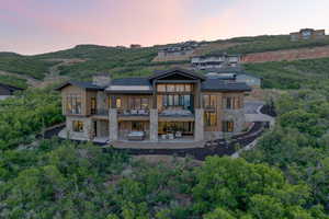 Back of property at dusk featuring stone siding, a balcony, a patio, and a chimney