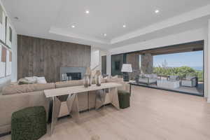 Living area featuring a fireplace, wood walls, light wood-type flooring, recessed lighting, and a raised ceiling