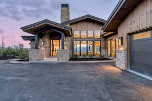Exterior entry at dusk with stone siding, a chimney, asphalt driveway, and a garage
