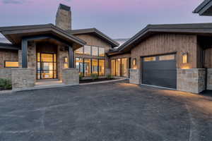 View of front facade featuring a chimney, stone siding, an attached garage, and driveway