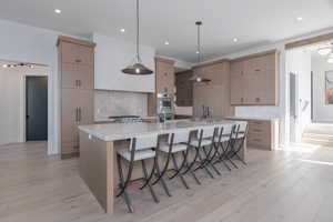 Kitchen with a breakfast bar, tasteful backsplash, a large island, modern cabinets, and light wood-type flooring