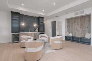 Living room featuring wine cooler, light wood-style flooring, a tray ceiling, bar with sink, and recessed lighting