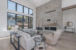 Living room with high vaulted ceiling, plenty of natural light, wood finished floors, a stone fireplace, and recessed lighting