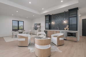 Living area with wine cooler, light wood-style flooring, a raised ceiling, recessed lighting, and wet bar