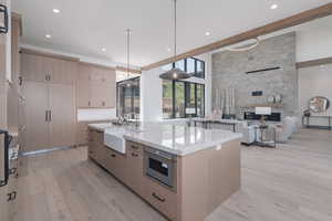 Kitchen with light brown cabinets, light wood-style flooring, an island with sink, light stone countertops, and a fireplace