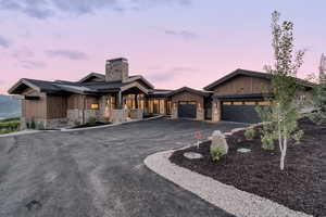 View of front of house featuring a garage, a chimney, stone siding, driveway, and a porch