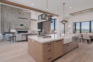 Kitchen with open floor plan, light wood-style floors, beam ceiling, hanging light fixtures, and light stone counters