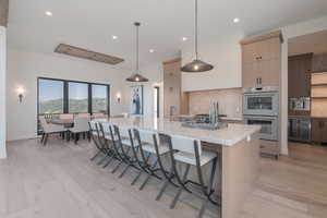 Kitchen featuring stainless steel double oven, light wood-style flooring, backsplash, a spacious island, and a breakfast bar area