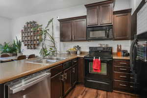 Kitchen featuring dark hardwood / wood-style flooring, sink, dark brown cabinetry, and black appliances