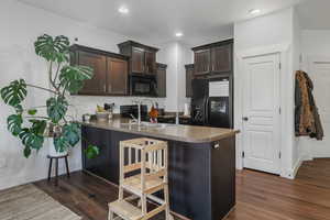 Kitchen with kitchen peninsula, dark brown cabinets, sink, and black appliances