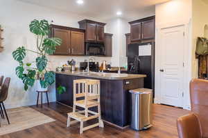 Kitchen with dark brown cabinetry, dark hardwood / wood-style floors, kitchen peninsula, and black appliances