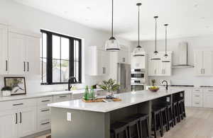 Kitchen with appliances with stainless steel finishes, wall chimney range hood, decorative light fixtures, white cabinetry, and a large island