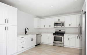 Kitchen featuring light stone counters, stainless steel appliances, sink, light hardwood / wood-style flooring, and white cabinetry