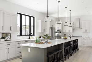 Kitchen featuring white cabinets, wall chimney range hood, a kitchen island with sink, and stainless steel appliances