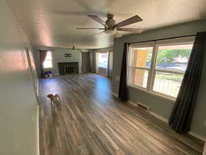 Unfurnished living room with a textured ceiling, dark hardwood / wood-style floors, and ceiling fan