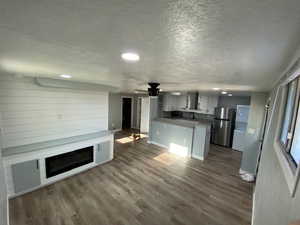 Unfurnished living room featuring ceiling fan, dark wood-type flooring, and a textured ceiling