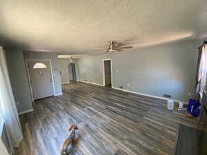 Unfurnished living room featuring a textured ceiling, ceiling fan, a barn door, and dark wood-type flooring