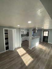 Kitchen with exhaust hood, kitchen peninsula, white cabinets, and dark wood-type flooring