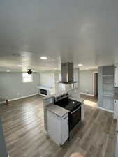 Kitchen featuring island exhaust hood, light wood-type flooring, white cabinetry, and stainless steel range with electric stovetop