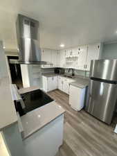 Kitchen featuring sink, light hardwood / wood-style floors, island range hood, white cabinets, and appliances with stainless steel finishes