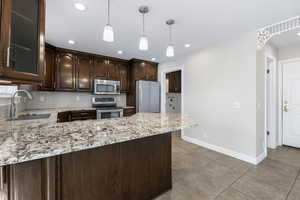 Kitchen with sink, stainless steel appliances, tasteful backsplash, light stone counters, and dark brown cabinets