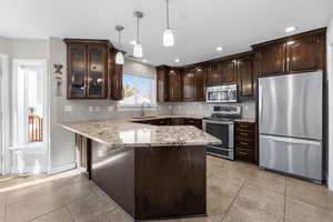 Kitchen with dark brown cabinetry, sink, hanging light fixtures, stainless steel appliances, and kitchen peninsula