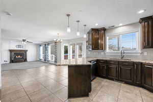 Kitchen featuring kitchen peninsula, dark brown cabinetry, ceiling fan with notable chandelier, sink, and pendant lighting