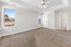 Spare room featuring a tray ceiling, ceiling fan, and light colored carpet