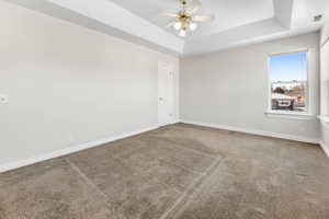 Carpeted spare room with ceiling fan and a raised ceiling