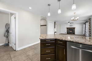 Kitchen featuring light stone counters, dark brown cabinets, ceiling fan, pendant lighting, and dishwasher