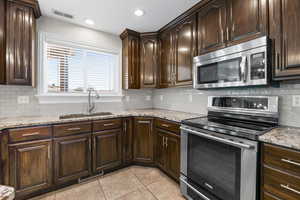 Kitchen featuring sink, light stone countertops, appliances with stainless steel finishes, tasteful backsplash, and dark brown cabinetry