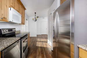 Kitchen with hanging light fixtures, dark hardwood / wood-style floors, a notable chandelier, light stone counters, and stainless steel appliances