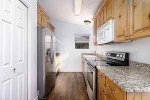 Kitchen featuring light stone countertops, stainless steel appliances, dark wood-type flooring, and sink