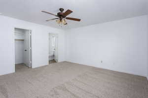 Unfurnished bedroom with ceiling fan, ensuite bathroom, light colored carpet, a walk in closet, and a closet