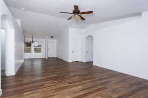 Unfurnished living room featuring a textured ceiling, ceiling fan with notable chandelier, dark hardwood / wood-style floors, and vaulted ceiling