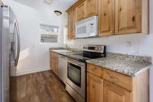 Kitchen with dark hardwood / wood-style flooring, light stone countertops, sink, and stainless steel appliances