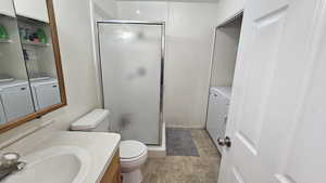 Bathroom featuring vanity, toilet, washing machine and dryer, and a shower with door