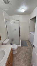 Bathroom with vanity, toilet, a textured ceiling, walk in shower, and washing machine and clothes dryer