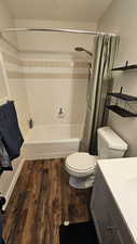 Full bathroom with vanity, toilet, shower / bathtub combination with curtain, a textured ceiling, and wood-type flooring