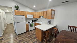 Kitchen with kitchen peninsula, dark hardwood / wood-style flooring, white appliances, sink, and lofted ceiling