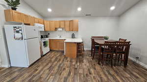 Kitchen with a breakfast bar, white appliances, dark wood-type flooring, sink, and lofted ceiling