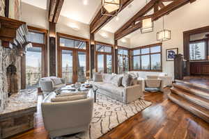 Living room featuring high vaulted ceiling, french doors, a stone fireplace, dark hardwood / wood-style floors, and beam ceiling