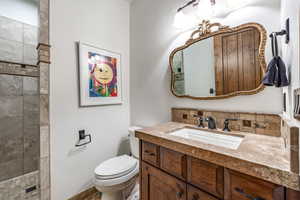 Bathroom with decorative backsplash, vanity, tiled shower, and toilet