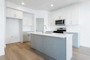 Kitchen with white cabinets, stainless steel appliances, a kitchen island with sink, and sink