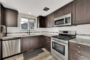 Kitchen with light stone counters, sink, dark brown cabinets, and stainless steel appliances