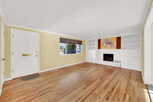 Unfurnished living room featuring a fireplace, built in shelves, light hardwood / wood-style flooring, and ornamental molding