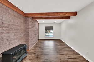 Unfurnished living room featuring a wood stove, beamed ceiling, and dark hardwood / wood-style floors