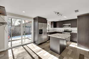 Kitchen featuring sink, appliances with stainless steel finishes, tasteful backsplash, dark brown cabinets, and a kitchen island